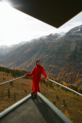 red-dress-woman-leaning-against-glass-corner-alpine-environment-fall-colors 